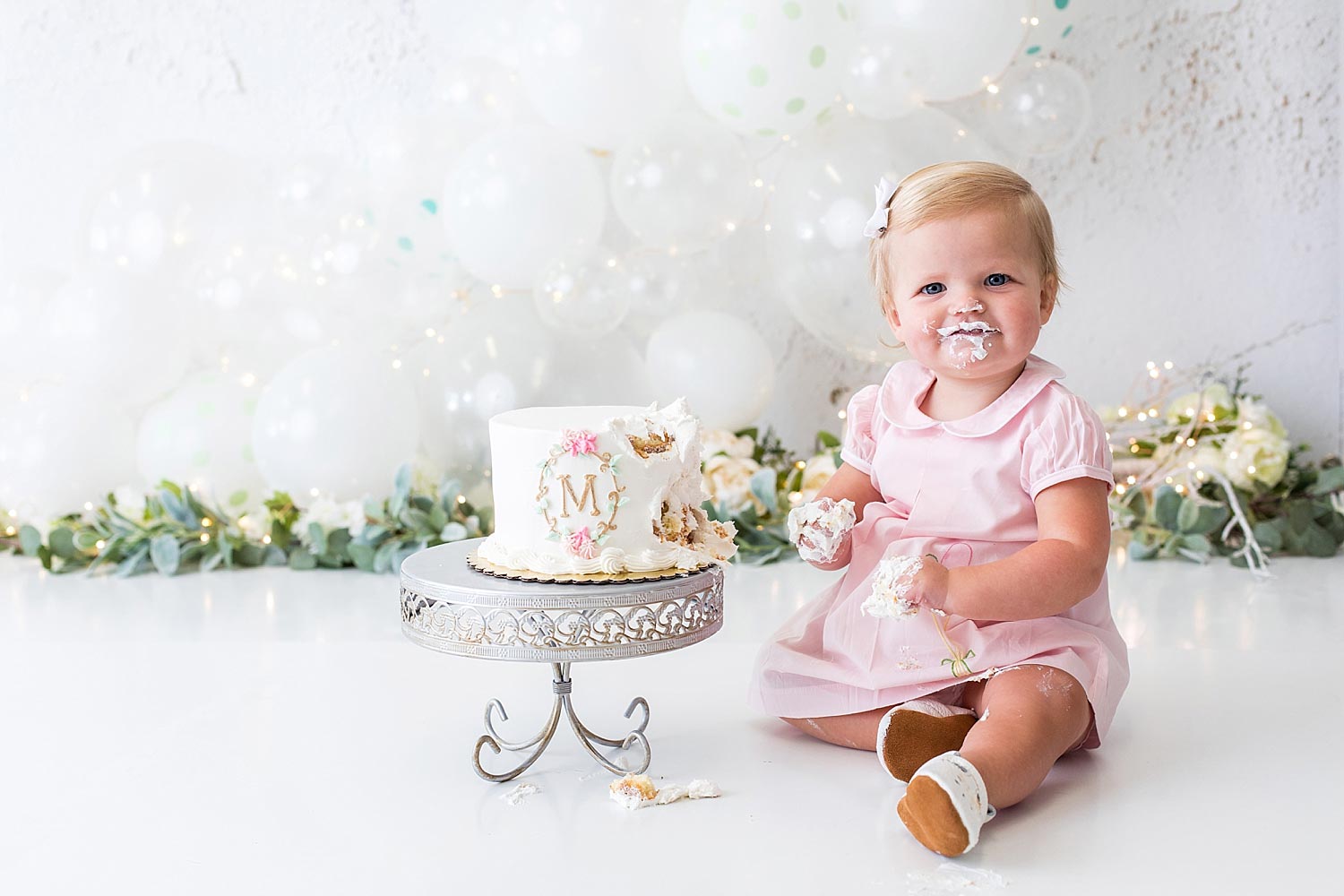 One-year-old girl in pink dress smiles with cake smashed on her face
