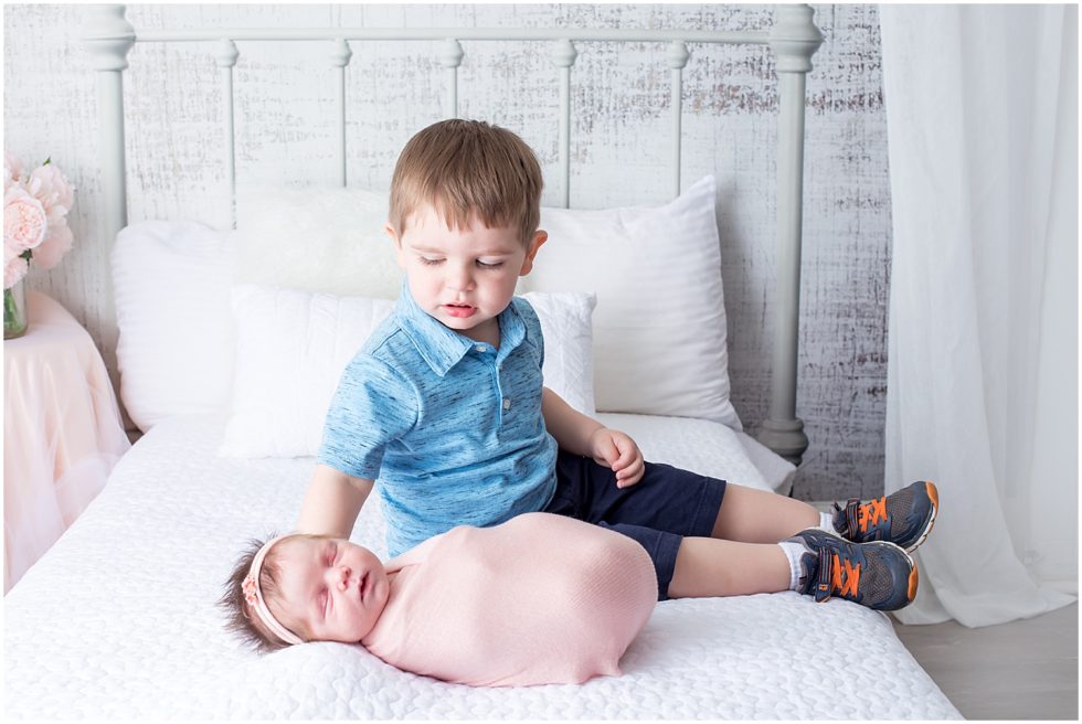 toddler brother sits with newborn sister