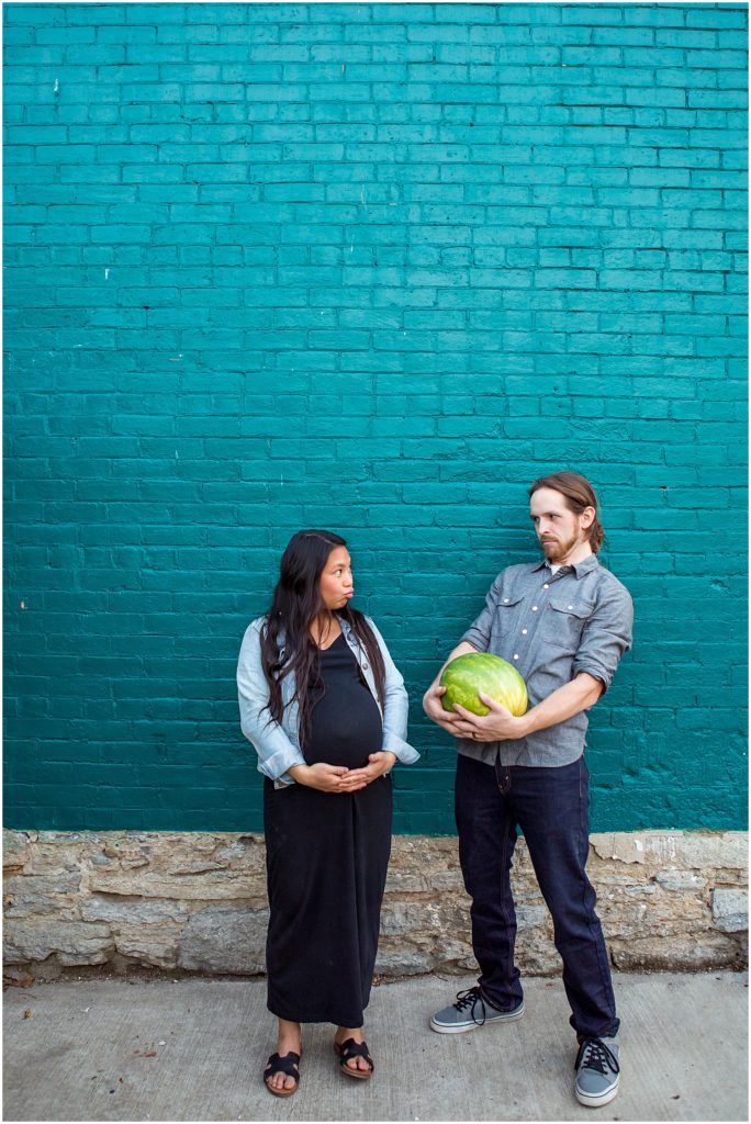 husband holds watermelon in comparison to wifes pregnant belly