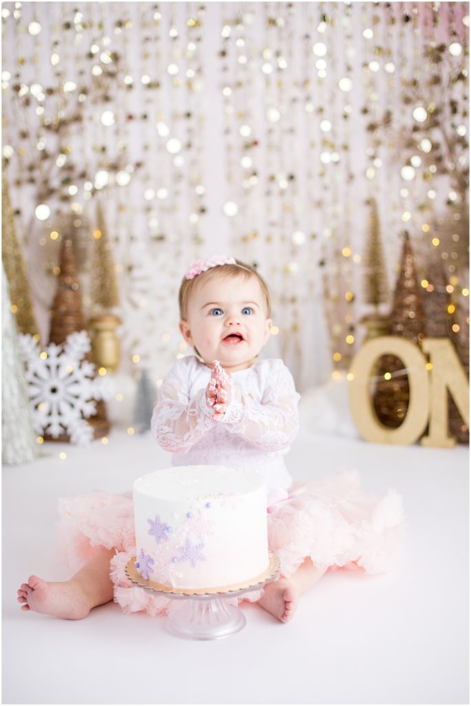 baby girl sits with pastel and gold birthday cake winter wonderland