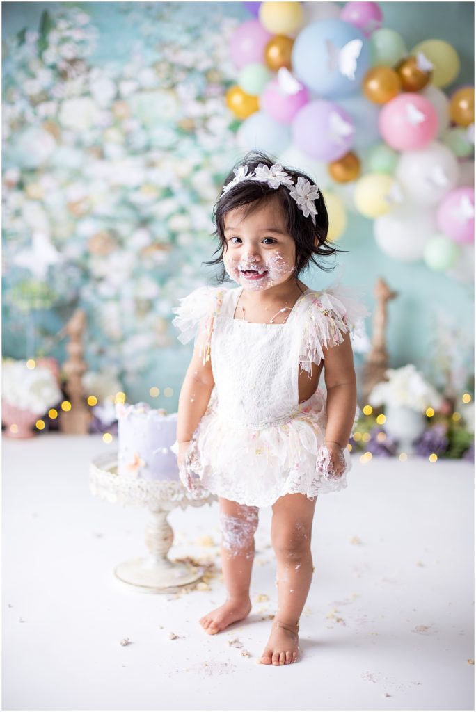 baby girl in white eyelet jumper covered in cake