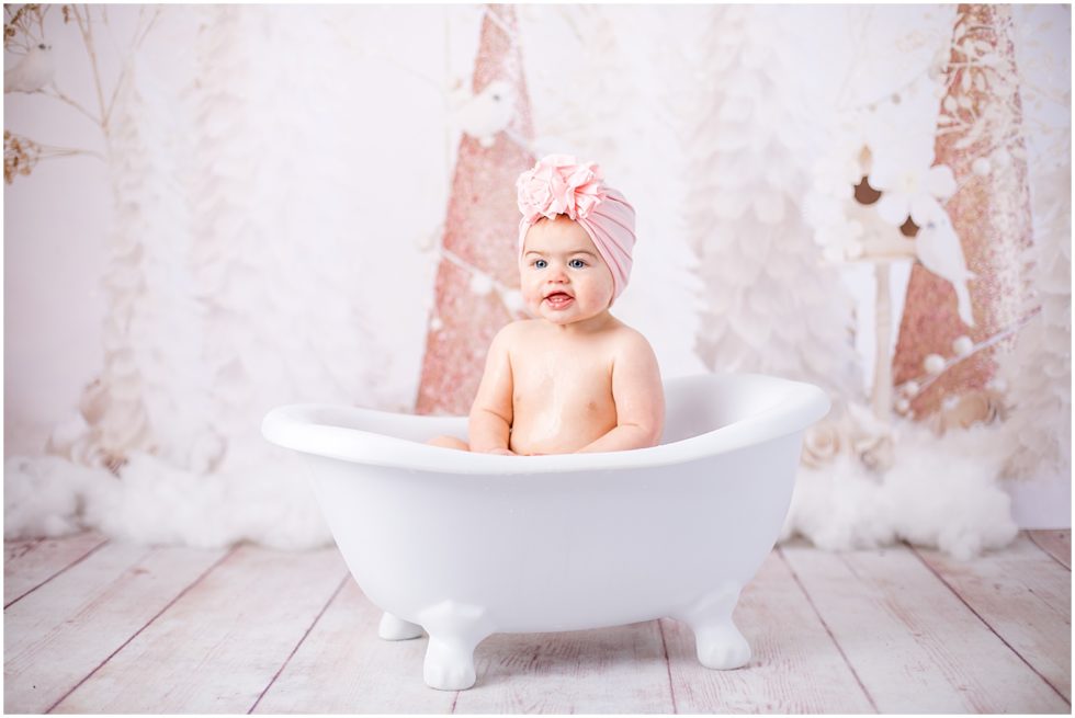 baby girl sits in little bathtub with pink head wrap on