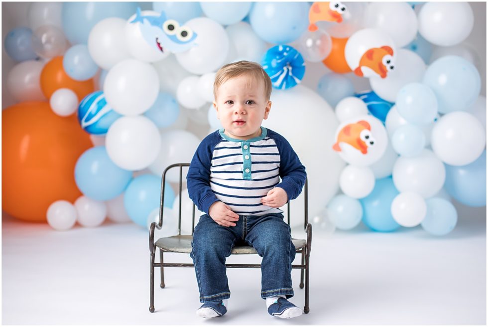 baby boy with blue striped shirt sits in chair with baby shark backgound