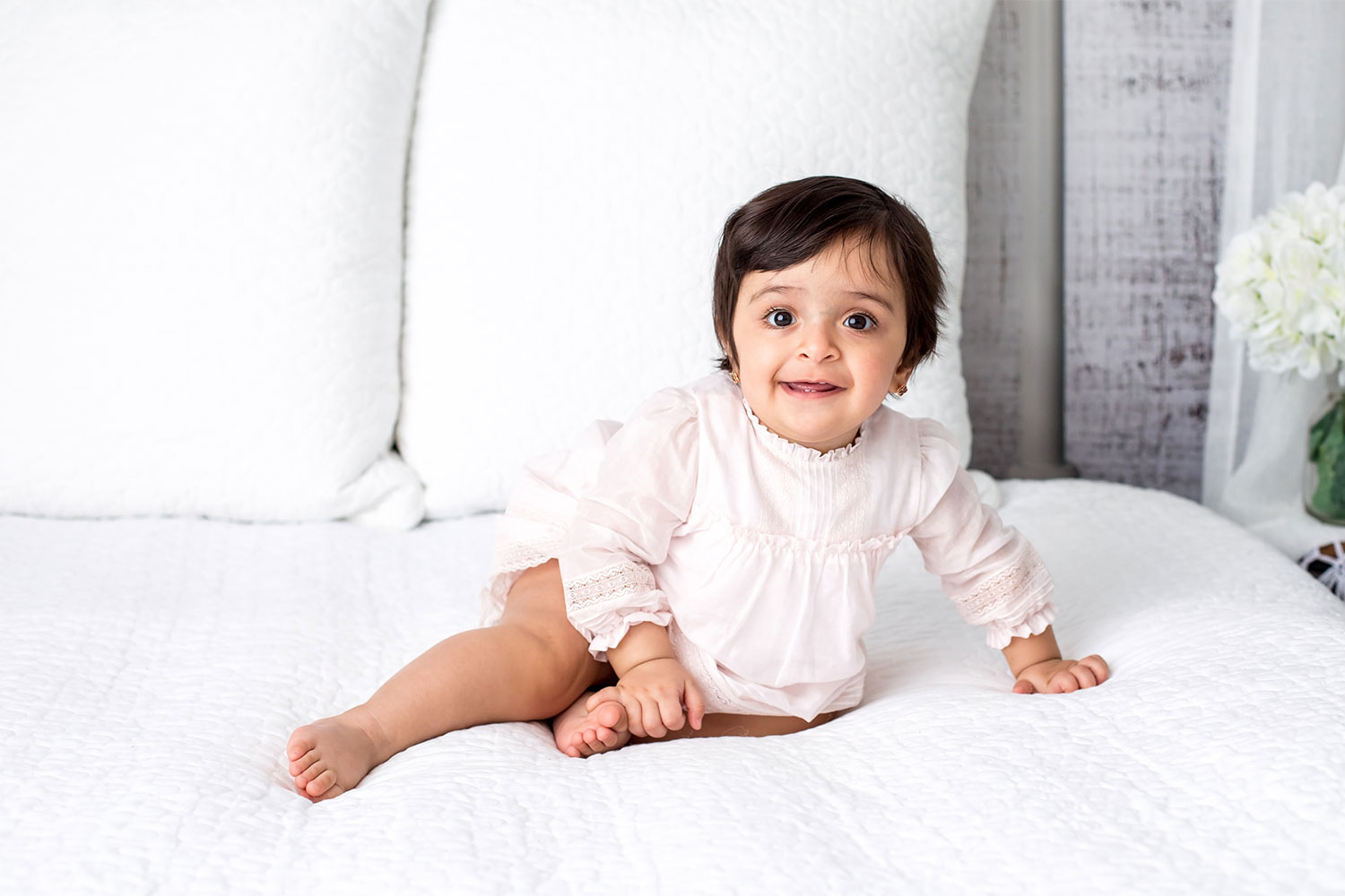 One year old girl sits on white bed