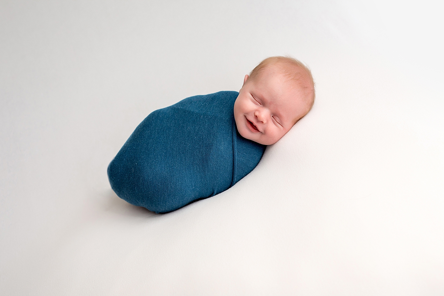 newborn baby smiles while sleeping in blue swaddle.jpg