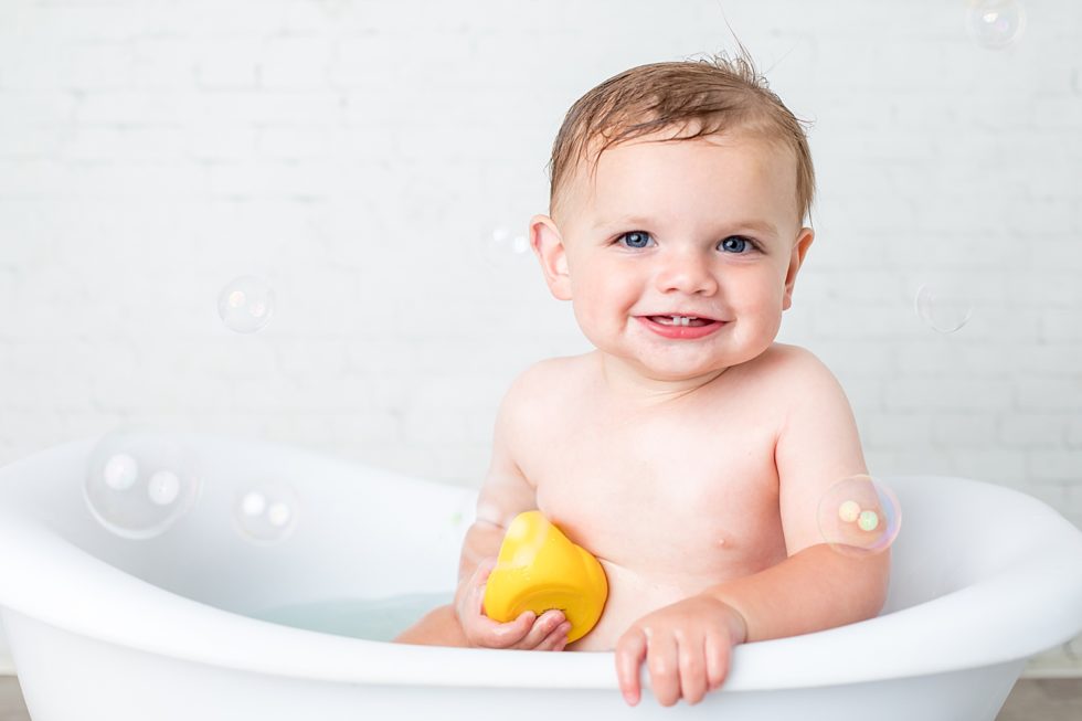 Baby sits in tub with yellow rubber ducky