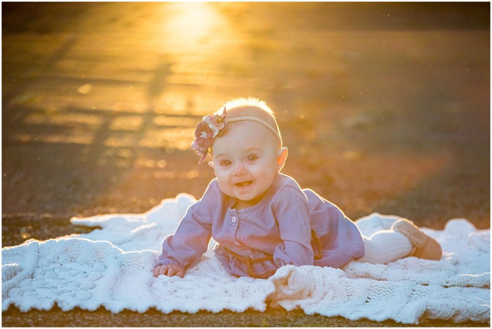 six month old baby lays on blanket in sunset