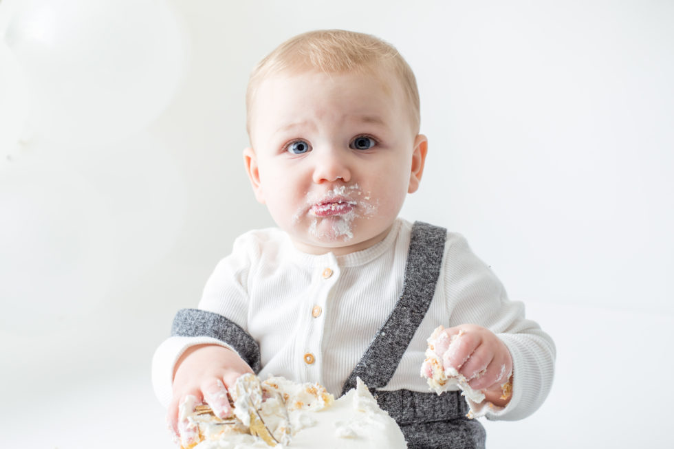 baby boy looks startled while digging in cake
